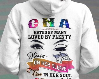May include: White hoodie with colorful text and graphics. The back of the hoodie features the letters "CNA" in rainbow colors, along with the phrases "Hated by Many, Loved by Plenty," and "Heart on Her Sleeve." Additional text includes "Fire in Her Soul and a Mouth She Can't Control."