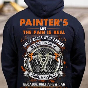 May include: Navy blue hooded sweatshirt with orange text that reads "PAINTER'S LIFE THE PAIN IS REAL THESE SCARS WERE EARNED MY CRAFT IS ONE OF PRIDE & RESPECT BECAUSE ONLY A FEW CAN DO WHAT I CAN." The design includes paint sprayers.