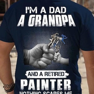 May include: Navy blue t-shirt with white text that reads "I'M A DAD, A GRANDPA, AND A RETIRED PAINTER, NOTHING SCARES ME." The shirt features a graphic of a hand holding a paint sprayer with a child's hand.