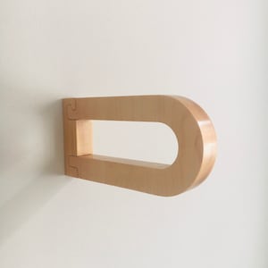 May include: A light wood wall-mounted towel bar with a rounded shape. The bar is made of natural wood and has a simple, modern design.