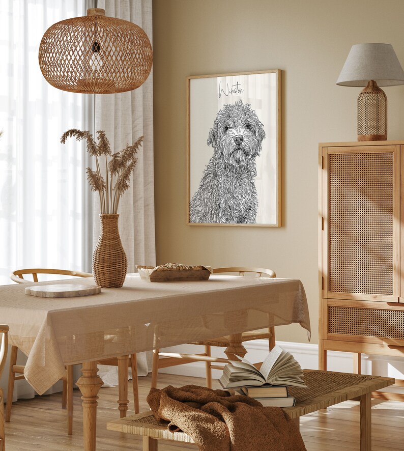 May include: A black and white line drawing of a dog named Winston on a woodgrain background. The drawing is framed and hanging on a wall in a dining room with a wooden table, chairs, and a woven lampshade.