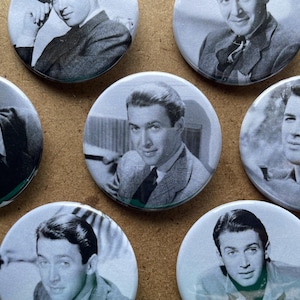 May include: A collection of black and white pinback buttons featuring portraits of a man in various poses. The buttons are round and have a glossy finish, with a classic, vintage aesthetic.