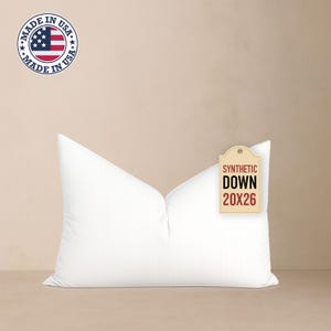May include: A white synthetic down pillow with a tag that reads "SYNTHETIC DOWN 20X26". The pillow is made in the USA, as indicated by a circular emblem with the American flag.