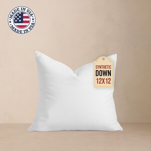 May include: A white square pillow with a tag that reads "SYNTHETIC DOWN 12X12". The pillow is made in the USA, as indicated by a circular sticker with the American flag and the text "MADE IN USA".
