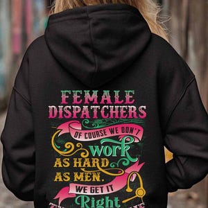 Pode incluir: Moletom preto com o texto "FEMALE DISPATCHERS" em rosa e verde. O design inclui as frases "OF COURSE WE DON'T work AS HARD AS MEN. WE GET IT Right THE FIRST TIME" e um gráfico de fone de ouvido.