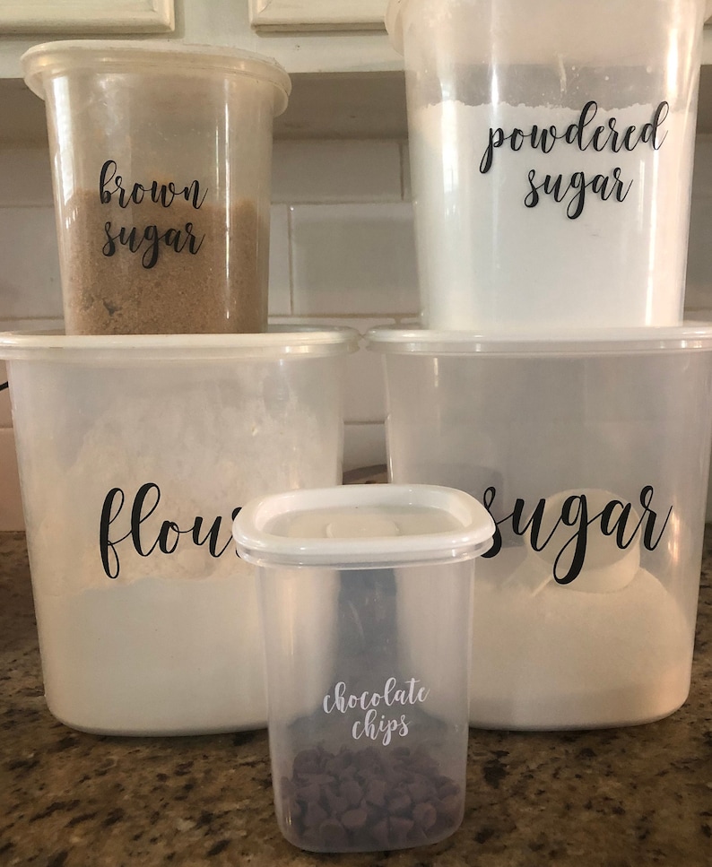 May include: Five clear plastic containers with labels for baking ingredients. The containers are labeled "brown sugar", "powdered sugar", "flour", "sugar", and "chocolate chips".