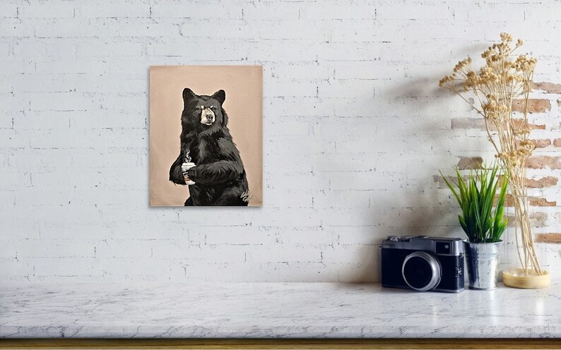 May include: A black bear holding a white coffee cup. The bear is standing on a light brown background.