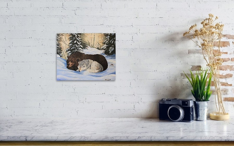 May include: A painting of a brown bear and a white wolf cuddling in a snowy forest setting. The bear is lying on its side with its head resting on the wolf's back. The wolf is curled up next to the bear, with its head resting on the bear's side. The forest is depicted in the background with trees and snow.