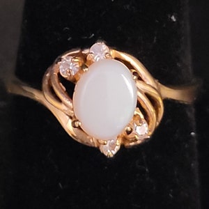 May include: A gold ring with a white oval gemstone surrounded by smaller clear gemstones.