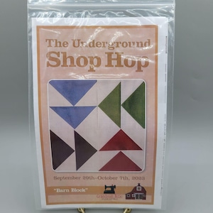 May include: A printed paper with the text "The Underground Shop Hop" and "Barn Block" is visible. The design features a quilt block with blue, green, and red triangles. The dates "September 29th-October 7th, 2023" are also printed on the paper.