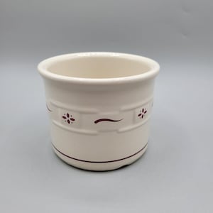 May include: A white ceramic butter dish with a burgundy floral design. The dish has a round shape and a slightly flared rim.
