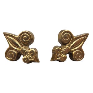 May include: A pair of gold-colored, ornate earrings. Each earring features a stylized floral design with swirling details and a textured finish. The earrings are presented against a white background.