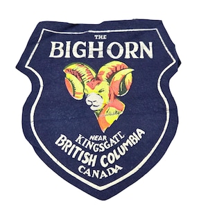 May include: A navy blue shield-shaped patch with white text and a colorful ram illustration. The text reads "THE BIGHORN" at the top, with "NEAR KINGSGATE BRITISH COLUMBIA CANADA" at the bottom. The ram is yellow, orange, and white.