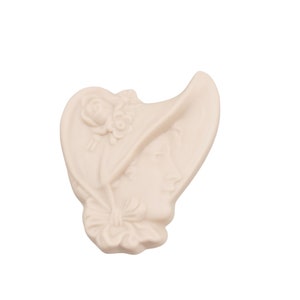 May include: A cream-colored cameo featuring a woman's profile wearing a bonnet adorned with a rose and floral details. The cameo has a heart-shaped design and a bow at the neck.