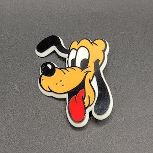 May include: A yellow and black cartoon dog with a red tongue sticking out. The dog has a black nose and white eyes.