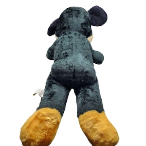 Puede incluir: Un gran juguete de peluche con forma de perro negro y verde con patas marrones. El perro est&aacute; acostado de espaldas con las patas en el aire.