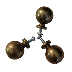 May include: Three antique brass cabinet knobs with a round ball design. Each knob has a small, decorative base and a screw for attachment. The knobs are a warm, golden color and appear to be vintage.