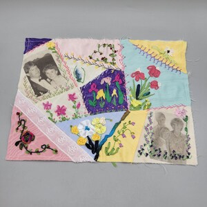 May include: A patchwork quilt with a variety of fabrics and colors, including pink, blue, yellow, and green. The quilt is decorated with embroidered flowers and two black and white photographs.