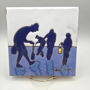 May include: A square ceramic tile featuring a stylised illustration of three dark blue figures against a white and light blue background. One figure holds a yellow lantern, while another carries a tool. The artist's signature is visible in the corner.