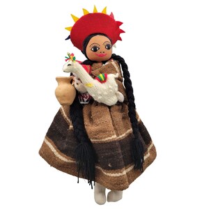 May include: A handmade doll wearing a brown and black striped skirt, a red hat with yellow and blue accents, and holding a white llama. The doll has black hair in braids and brown eyes.