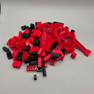 May include: A large pile of assorted plastic building bricks in vibrant red and solid black colors. The collection consists of various rectangular shapes and sizes, each featuring circular studs on the top surface for interlocking connection.