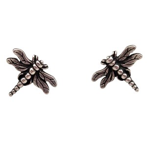 May include: A pair of silver-colored dragonfly stud earrings. Each earring features a detailed dragonfly design with textured wings and a segmented body. The earrings are set against a white background.