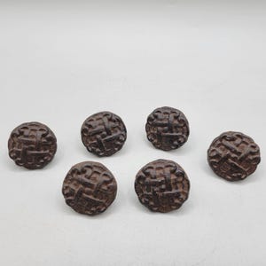 May include: A collection of six dark brown, round buttons with a woven texture. The buttons are evenly spaced against a white background, showcasing their intricate design and rustic appeal. These buttons are ideal for sewing and craft projects.