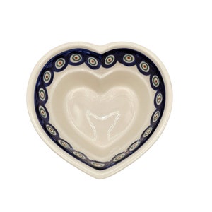 May include: A white ceramic heart-shaped bowl with a blue and red patterned rim. The bowl has a smooth, glossy finish.