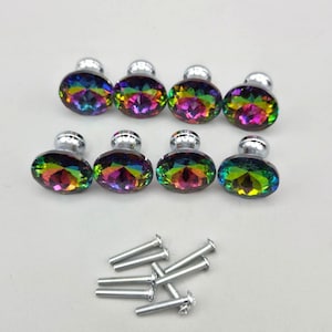 May include: Eight oval-shaped cabinet knobs featuring a faceted, iridescent rainbow finish with a metallic silver base. The set includes eight matching silver-colored metal screws for installation, arranged in a cluster below the knobs.