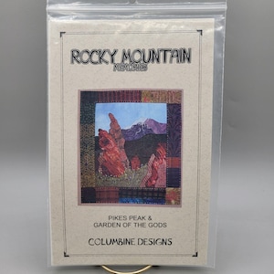 May include: A tan paper pattern with a brown border. The pattern is for a quilt featuring a mountain scene with a red rock formation in the foreground. The text reads "Rocky Mountain Memories", "Pikes Peak & Garden of the Gods", and "Columbine Designs".