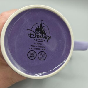 May include: A purple Disney Parks mug with a white rim and handle. The bottom of the mug features the Disney Parks logo, the text "&copy;Disney Made in Thailand", and other symbols.
