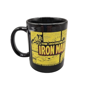 May include: Black ceramic mug with a yellow and black comic book design featuring Iron Man. The text "The Invincible Iron Man" is printed in red and yellow.