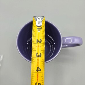 May include: A lavender ceramic mug with a matching handle. A yellow measuring tape is placed inside the mug, showing a height of approximately 4 inches. The mug has a glossy finish and a simple, classic design.