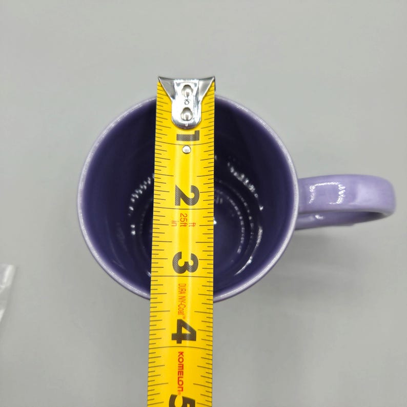 May include: A lavender ceramic mug with a matching handle. A yellow measuring tape is placed inside the mug, showing a height of approximately 4 inches. The mug has a glossy finish and a simple, classic design.