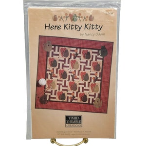 May include: Quilt pattern for a cat-themed quilt titled "Here Kitty Kitty" by Nancy Odom. The pattern features a quilt design with cats, hearts, and yarn balls.