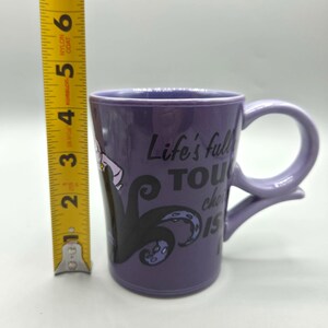 May include: Purple ceramic mug with a curved handle. The mug features a graphic of a character with black tentacles and the text "Life's full of tough choices, isn't it?" The mug is approximately 4 inches tall.
