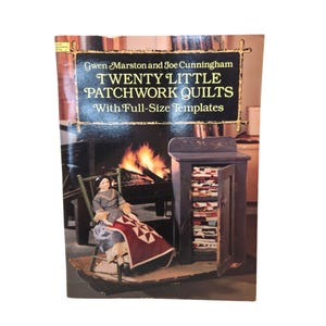 May include: A softcover book titled Twenty Little Patchwork Quilts With Full-Size Templates by Gwen Marston and Joe Cunningham. The cover features a doll sitting in a green wooden chair holding a small quilt, next to a small dark cabinet.