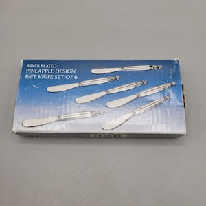 May include: A set of six silver-plated pate knives with a pineapple design. The knives are displayed in their original box, which has text that reads "Silver Plated Pineapple Design Pate Knife Set of 6."
