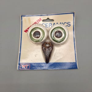 May include: Two round white ceramic pieces with green and brown centres and one brown teardrop-shaped ceramic piece on a Western Trimming Corp packaging card. The card features the text WESTRIM CERAMICS and WT logo with manufacturing details.