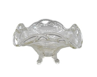 May include: A clear glass footed bowl with a scalloped edge and intricate cut-out design. The bowl is perfect for serving fruit, candy, or other small treats.
