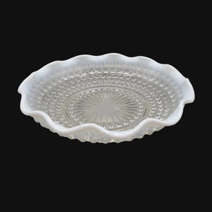 May include: A white, scalloped-edge glass bowl with a textured, hobnail pattern on the sides and a starburst design in the center. The bowl is likely vintage and sits against a black background.