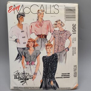 May include: McCall's Easy 3951 sewing pattern for tops. The pattern includes four different styles of tops, including a white top with buttons, a pink top with a draped neckline, a striped top with short sleeves, and a black and white patterned top with long sleeves. The pattern is for a medium size.