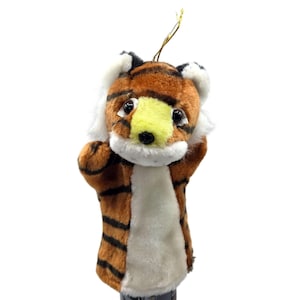 May include: A plush tiger hand puppet with a brown and black striped body, white chest, and a yellow and white face. The puppet has black eyes and a gold string for hanging. The puppet is designed to fit over the hand.