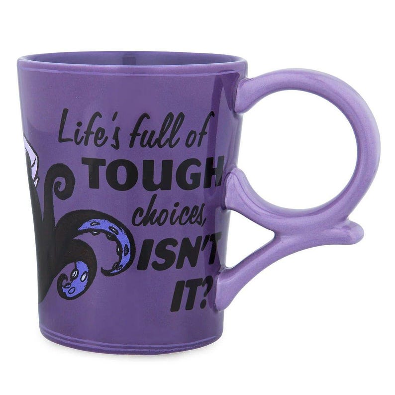 May include: Purple ceramic mug with a unique handle design. The mug features the text "Life's full of TOUGH choices, ISN'T IT?" along with a black and purple graphic. The handle is a loop shape.