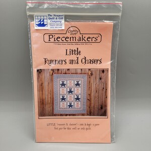 May include: A pink and blue quilt pattern with a design of bears running and chasing each other. The pattern is called "Little Runners and Chasers" and is from Piecemakers Country Store.