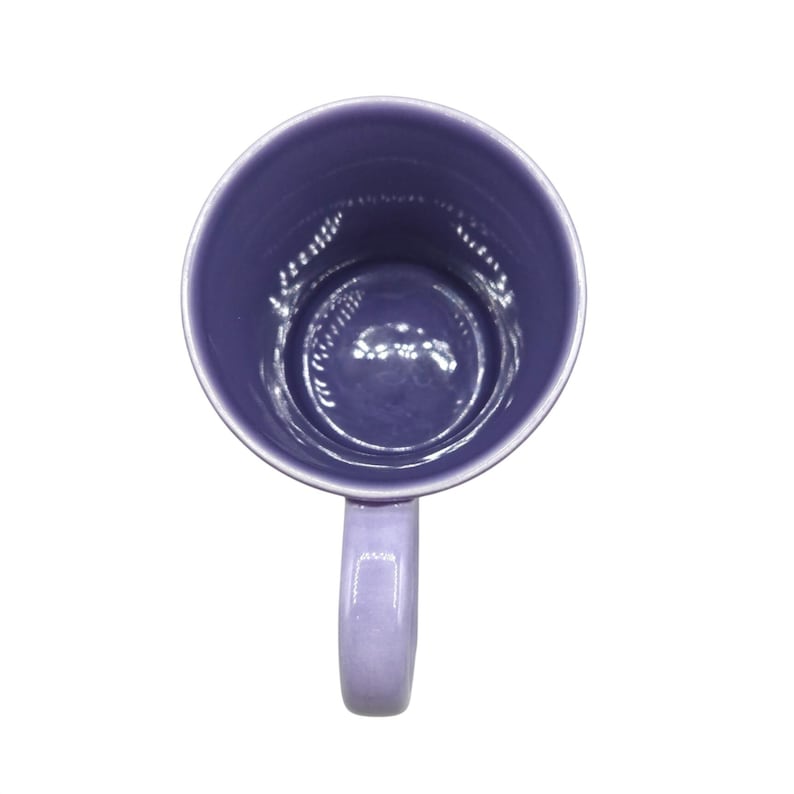 May include: A lavender ceramic mug viewed from above. The mug has a rounded body and a curved handle. The interior and exterior of the mug are the same shade of lavender. The mug is set against a white background.