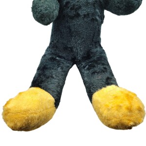 Puede incluir: Un gran juguete de peluche con forma de persona. El juguete lleva un mono verde oscuro con pies amarillos.