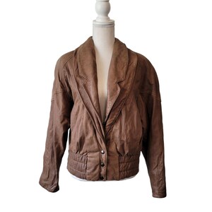May include: A brown leather jacket with a  collar, a button closure, and a cinched waist.