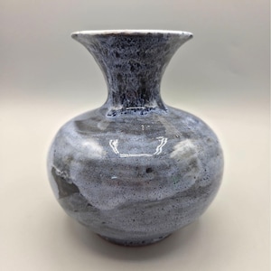 May include: A ceramic vase with a round body and a flared neck. The vase is primarily blue and gray with a speckled texture. The rim is white, and the overall design is smooth and glossy.