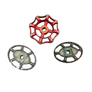 May include: Three vintage valve handles in the image. One is red, round, and has a square center. The other two are oval-shaped, with a square center, and are silver and green in color. All are made of metal.